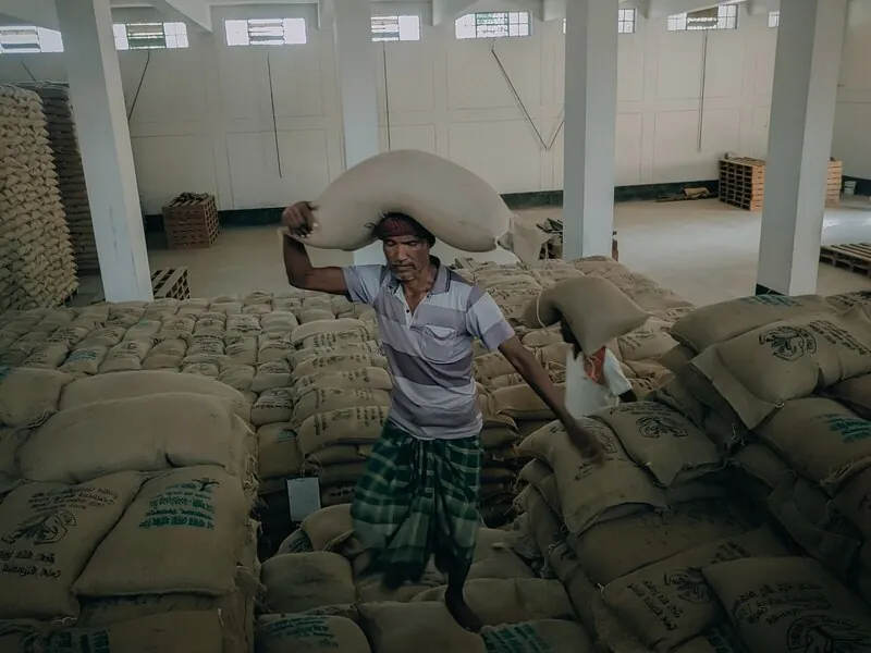 A worker moving 50 kg sacks in a bagged-goods storage facility