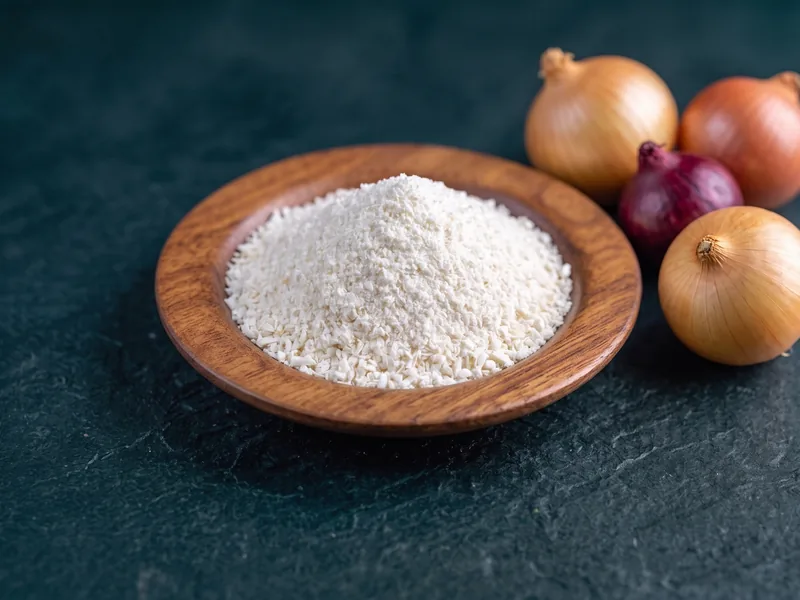 Dehydrated onion powder in a wooden dish, with white and red onions alongside